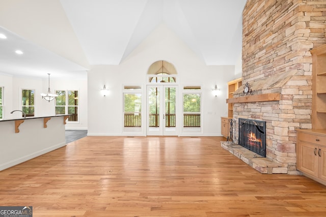 unfurnished living room featuring light hardwood / wood-style floors, a healthy amount of sunlight, high vaulted ceiling, and a fireplace