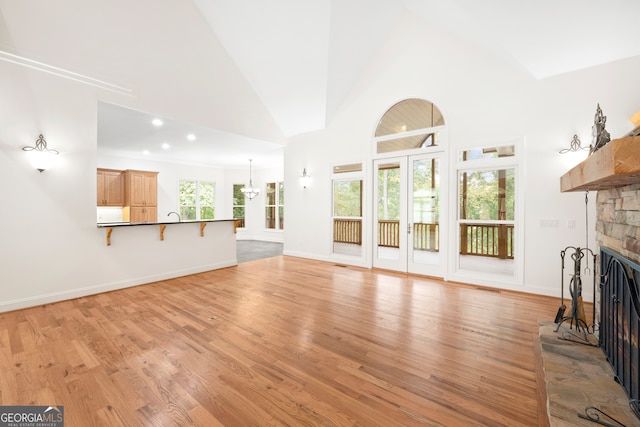 unfurnished living room featuring high vaulted ceiling, light hardwood / wood-style flooring, and a stone fireplace