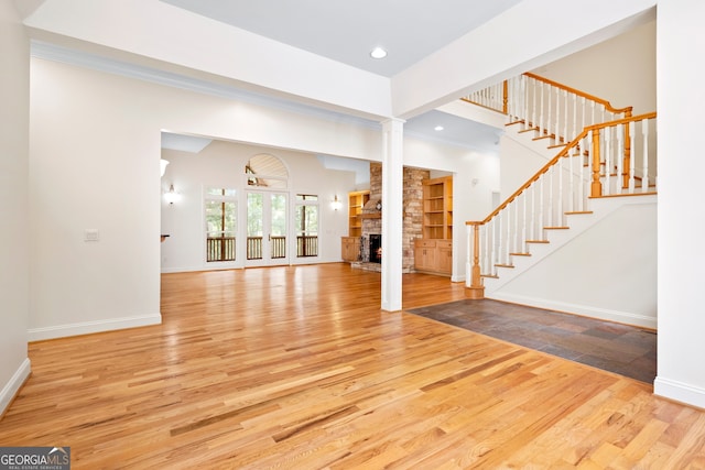 unfurnished living room featuring light hardwood / wood-style floors, a stone fireplace, and decorative columns