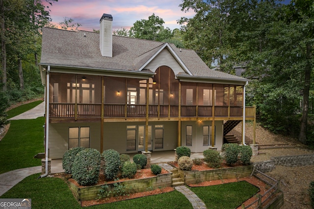 back house at dusk featuring a patio area, a lawn, and a sunroom