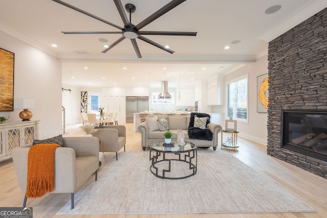 living room with crown molding, a stone fireplace, light hardwood / wood-style floors, and ceiling fan