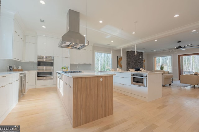 kitchen with a large island, plenty of natural light, white cabinets, island exhaust hood, and stainless steel double oven