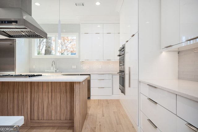 kitchen featuring pendant lighting, appliances with stainless steel finishes, light hardwood / wood-style floors, white cabinets, and island exhaust hood