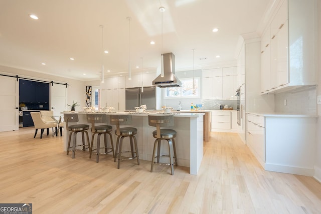 kitchen featuring a spacious island, stainless steel built in refrigerator, white cabinets, island exhaust hood, and a barn door