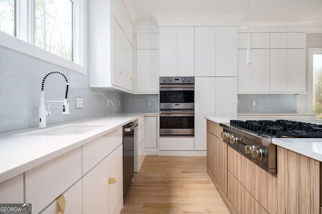 kitchen with sink, white cabinetry, light hardwood / wood-style flooring, stainless steel appliances, and backsplash