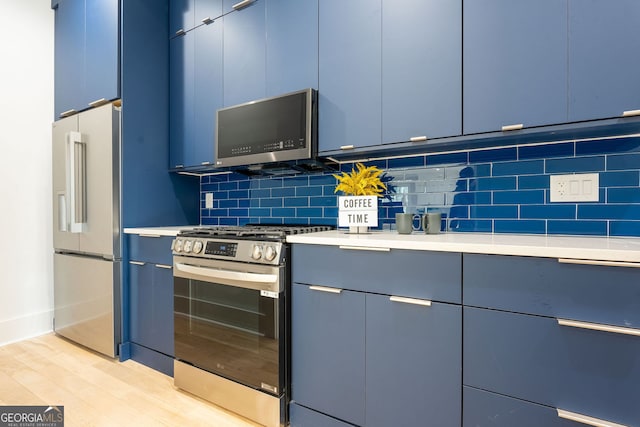 kitchen featuring blue cabinets, decorative backsplash, light wood-type flooring, and appliances with stainless steel finishes