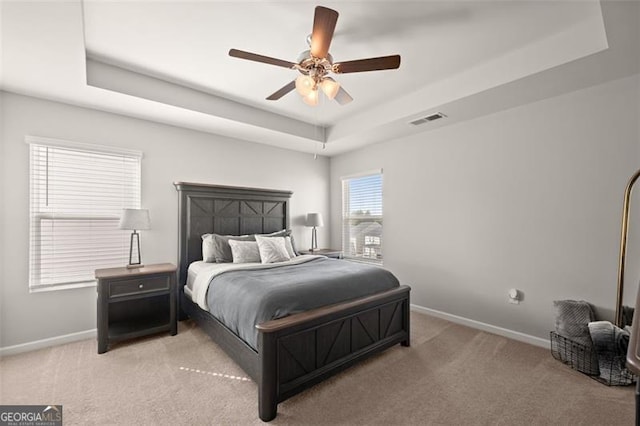 carpeted bedroom with ceiling fan and a tray ceiling