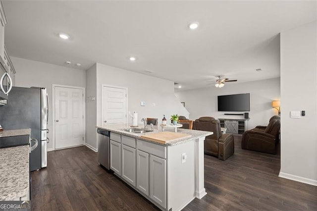 kitchen with sink, stainless steel appliances, dark wood-type flooring, light stone counters, and a center island with sink