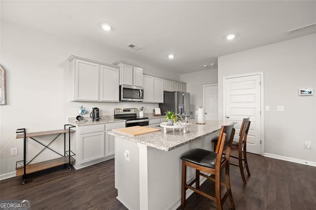 kitchen with appliances with stainless steel finishes, a center island with sink, a kitchen breakfast bar, and dark hardwood / wood-style flooring