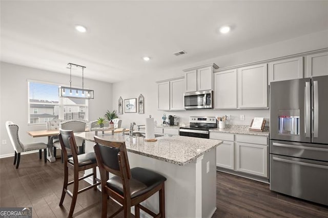 kitchen featuring a kitchen island with sink, sink, light stone countertops, appliances with stainless steel finishes, and dark hardwood / wood-style flooring