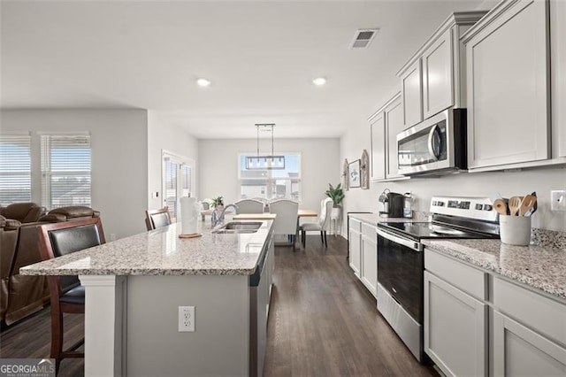 kitchen featuring a kitchen island with sink, dark wood-type flooring, hanging light fixtures, a breakfast bar, and appliances with stainless steel finishes