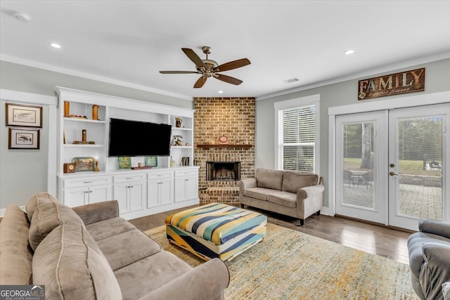 living room with french doors, wood-type flooring, crown molding, a brick fireplace, and ceiling fan