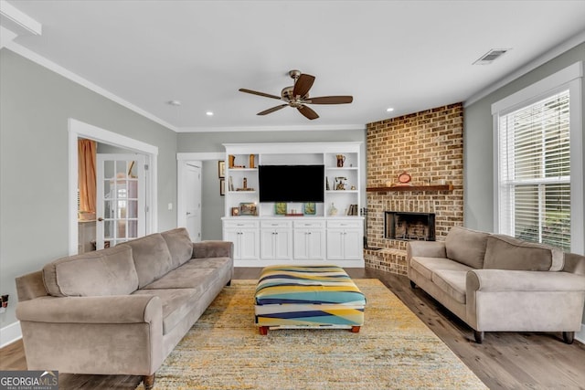 living room with ornamental molding, a brick fireplace, light wood-type flooring, and ceiling fan