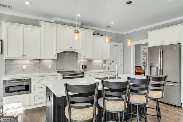 kitchen featuring decorative backsplash, white cabinetry, a kitchen island with sink, pendant lighting, and stainless steel appliances