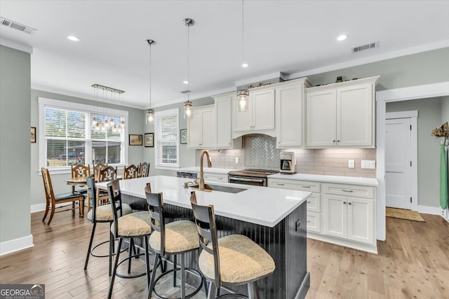 kitchen featuring decorative backsplash, hanging light fixtures, an island with sink, white cabinetry, and light hardwood / wood-style flooring