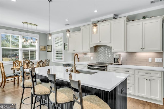 kitchen featuring a center island with sink, white cabinetry, decorative light fixtures, and electric stove