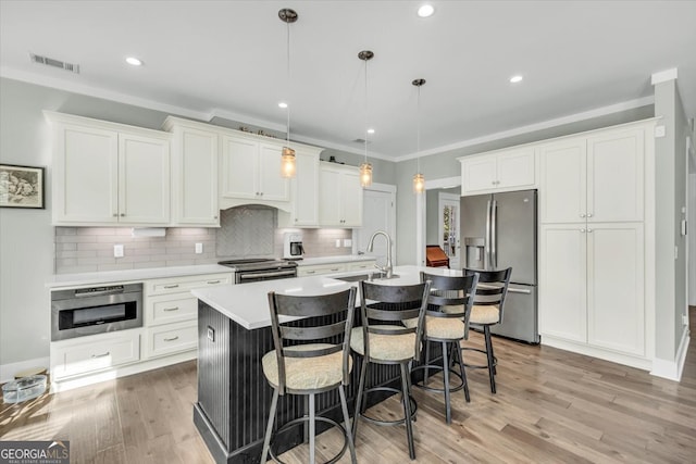 kitchen with white cabinets, a kitchen island with sink, pendant lighting, light hardwood / wood-style floors, and stainless steel appliances