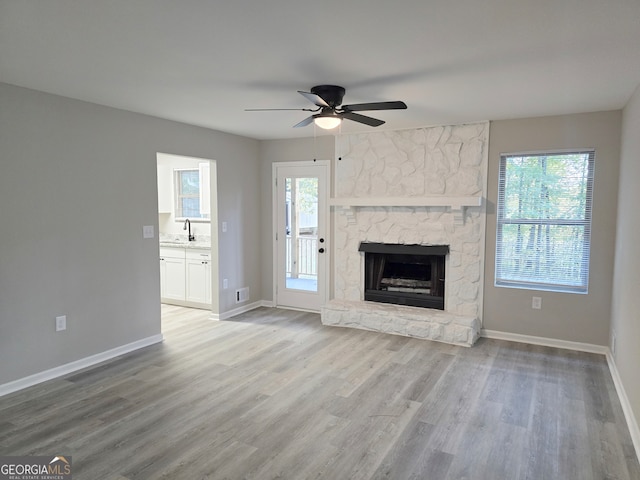 unfurnished living room with sink, a stone fireplace, light hardwood / wood-style floors, and ceiling fan