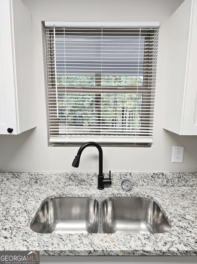 room details featuring sink, white cabinetry, and light stone counters