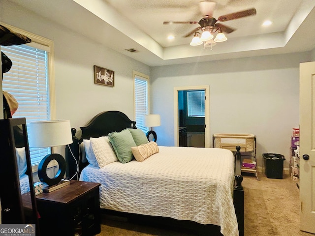 bedroom featuring multiple windows, carpet floors, ceiling fan, and a tray ceiling