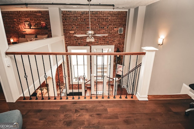 stairway with brick wall, wood-type flooring, and ceiling fan