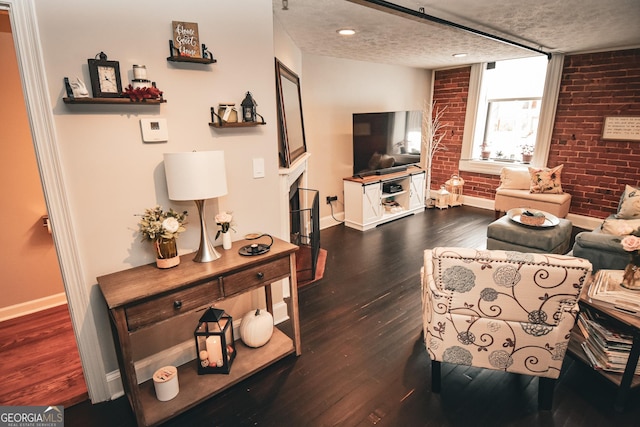 living room with a textured ceiling, dark hardwood / wood-style floors, and brick wall