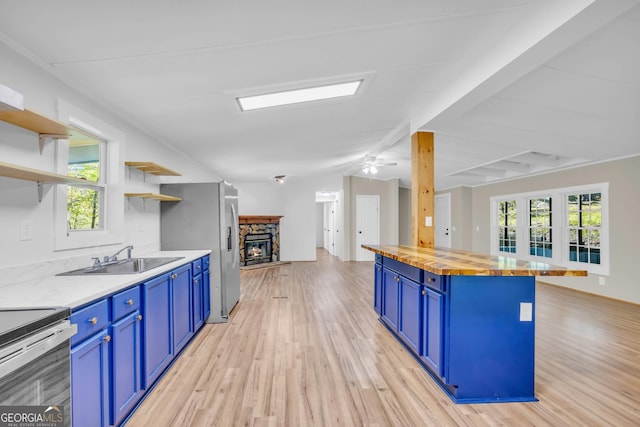 kitchen featuring ceiling fan, light wood-type flooring, butcher block counters, sink, and blue cabinets