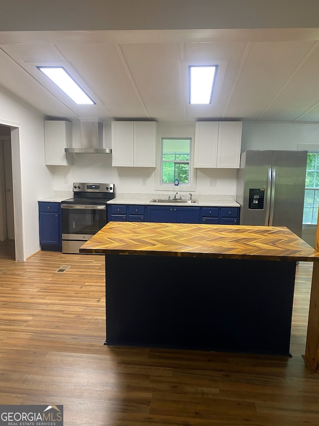 kitchen with blue cabinets, butcher block counters, stainless steel appliances, and white cabinetry