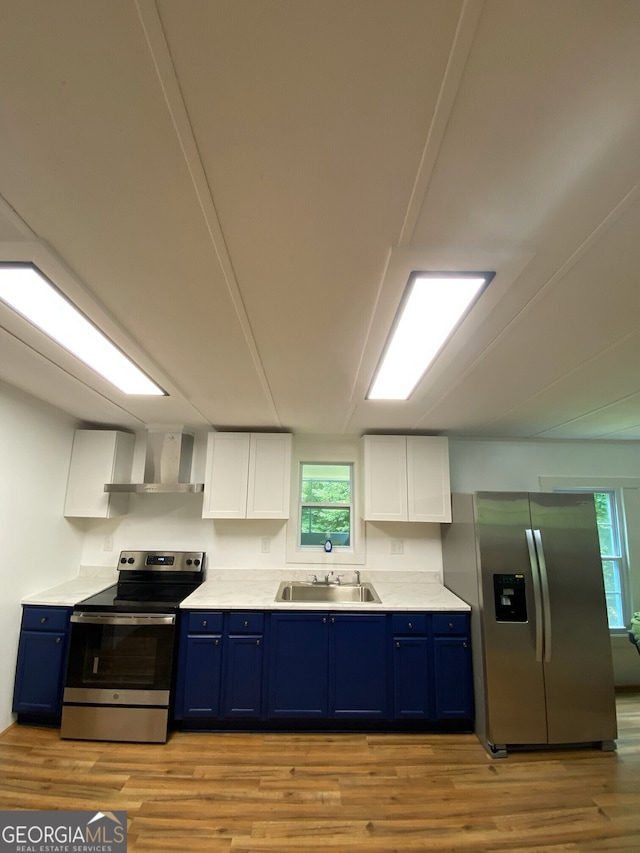 kitchen featuring wall chimney exhaust hood, blue cabinetry, white cabinetry, and stainless steel appliances