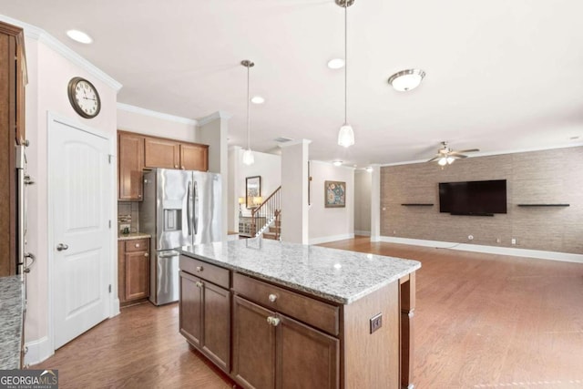 kitchen with light stone countertops, ceiling fan, stainless steel refrigerator with ice dispenser, decorative light fixtures, and a kitchen island