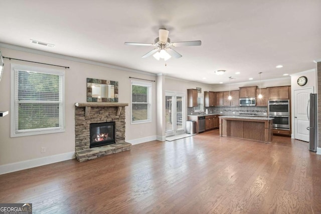 unfurnished living room featuring a stone fireplace, a wealth of natural light, dark wood-type flooring, and ornamental molding