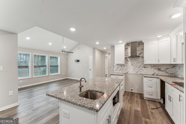 kitchen with white cabinets, wall chimney range hood, sink, vaulted ceiling, and light stone countertops