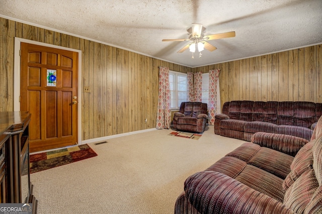 living room with a textured ceiling, wood walls, ceiling fan, and carpet floors