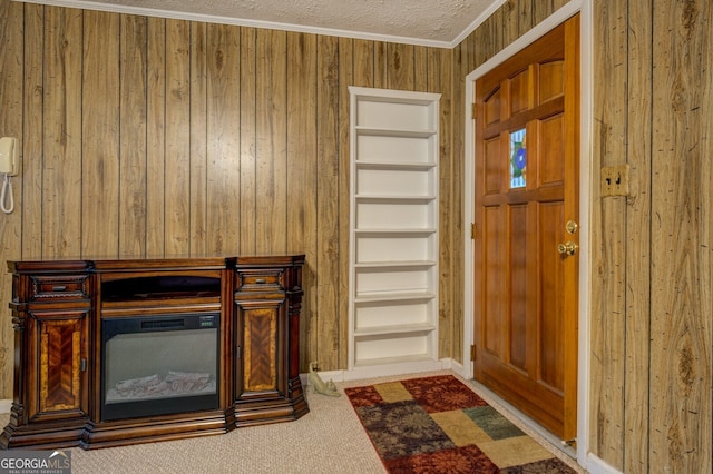 carpeted foyer entrance with wooden walls, a textured ceiling, and crown molding