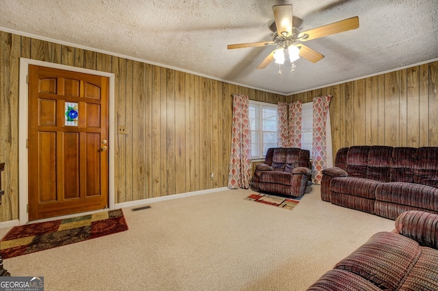 carpeted living room with wood walls, ceiling fan, a textured ceiling, and ornamental molding