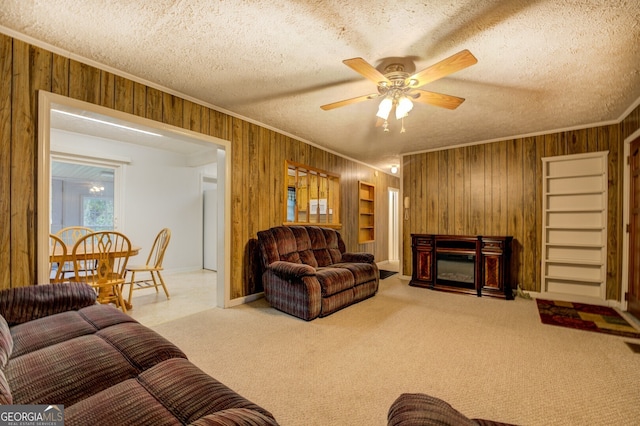 carpeted living room with wooden walls, a textured ceiling, ceiling fan, and crown molding