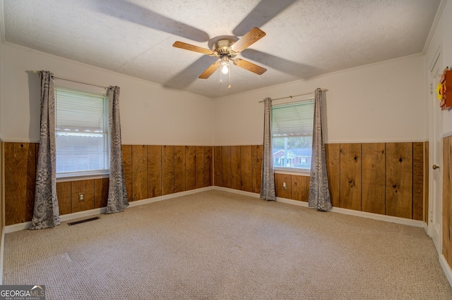 unfurnished room featuring ceiling fan, wooden walls, light carpet, and a textured ceiling