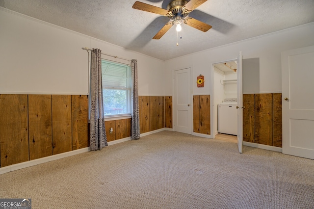 unfurnished bedroom featuring washer / dryer, ceiling fan, wooden walls, and a textured ceiling