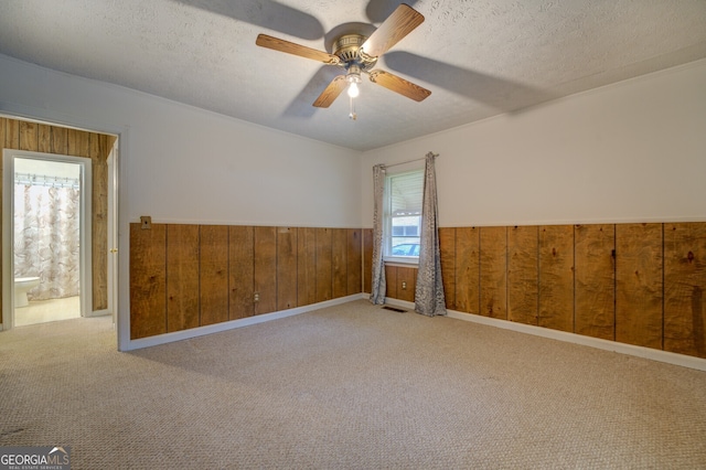 carpeted spare room with wooden walls, a textured ceiling, and ceiling fan