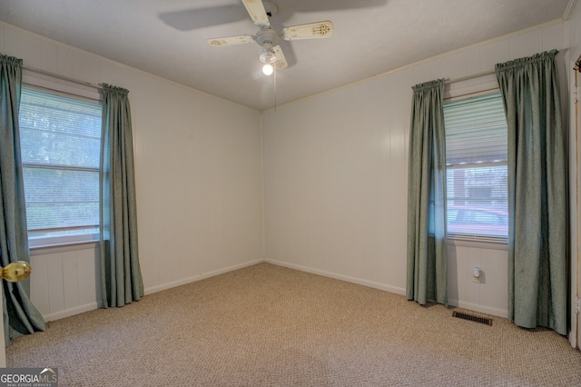 carpeted spare room featuring ornamental molding, a wealth of natural light, and ceiling fan