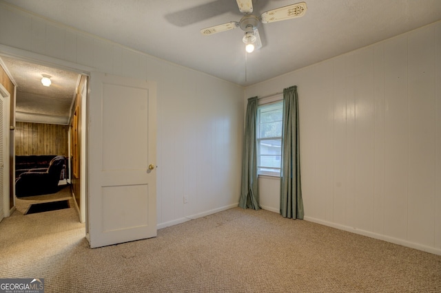 unfurnished bedroom with wooden walls, light carpet, and ceiling fan