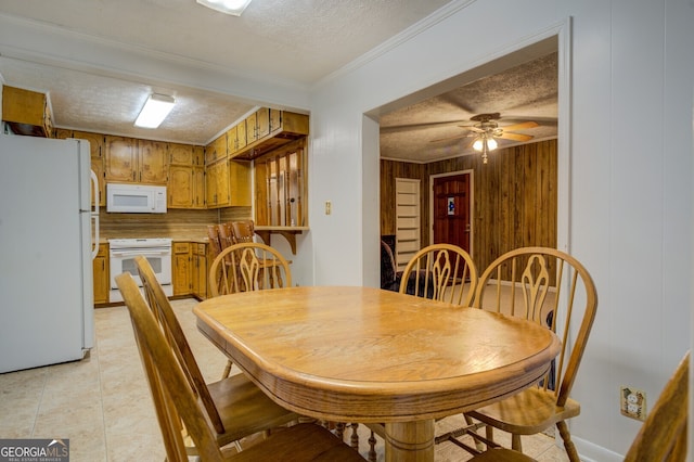 dining area with light tile patterned flooring, ornamental molding, a textured ceiling, wooden walls, and ceiling fan