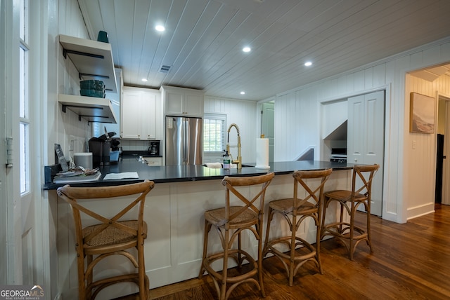 kitchen featuring white cabinets, stainless steel refrigerator, dark hardwood / wood-style floors, and kitchen peninsula