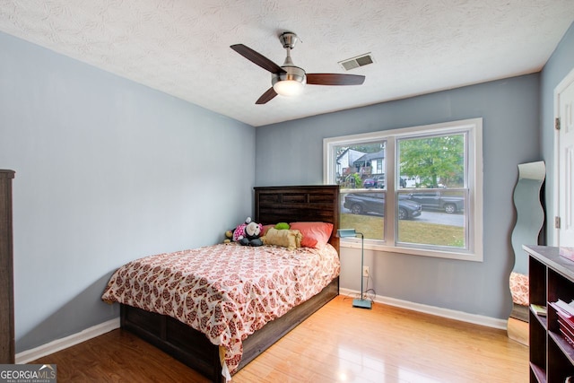 bedroom with a textured ceiling, hardwood / wood-style flooring, and ceiling fan