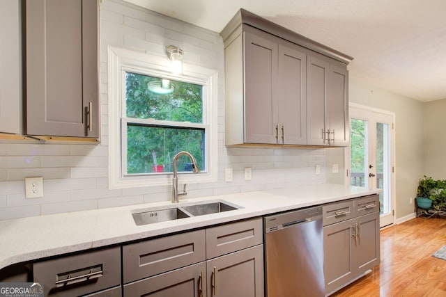 kitchen with stainless steel dishwasher, a wealth of natural light, decorative backsplash, and light wood-type flooring