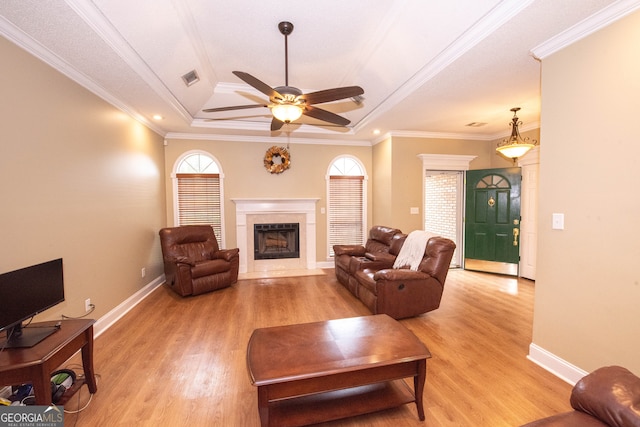 living room featuring ceiling fan, a tray ceiling, ornamental molding, and light hardwood / wood-style flooring