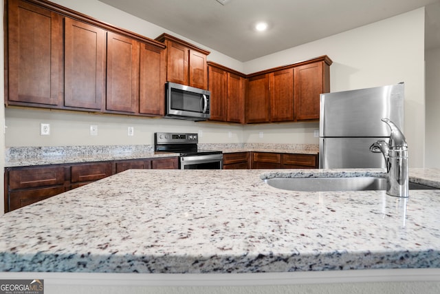 kitchen with stainless steel appliances, sink, and light stone counters