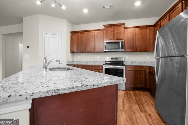 kitchen with light hardwood / wood-style floors, a kitchen island with sink, and appliances with stainless steel finishes