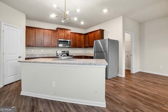 kitchen featuring dark wood-type flooring, pendant lighting, appliances with stainless steel finishes, and a center island with sink