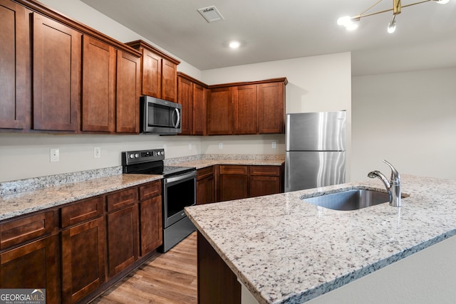 kitchen featuring stainless steel appliances, a kitchen island, light stone countertops, sink, and light hardwood / wood-style flooring